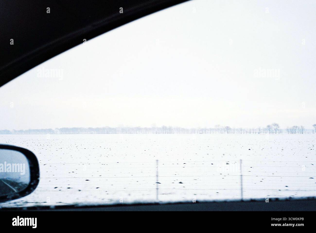 Foto analogica attraverso il finestrino della porta del passeggero di un'auto in movimento su un'autostrada nebbiosa e innevata. Barriera stradale visibile. Atmosfera invernale tranquilla e fredda. Foto Stock