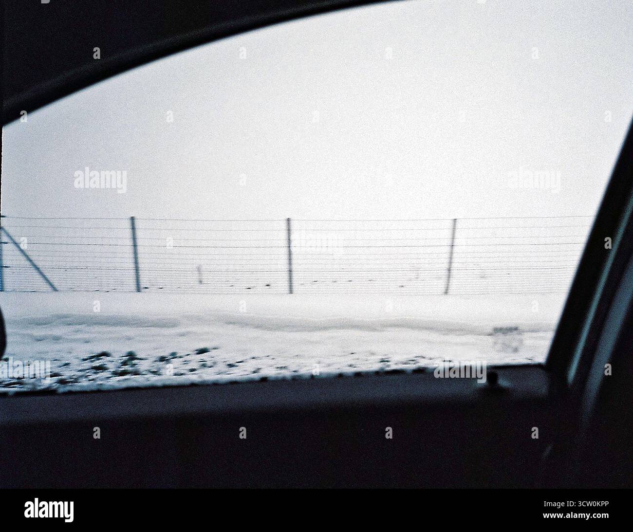 Foto analogica attraverso il finestrino della porta del passeggero di un'auto in movimento su un'autostrada nebbiosa e innevata. Barriera stradale visibile. Atmosfera invernale tranquilla e fredda. Foto Stock