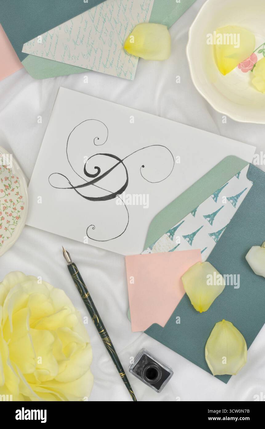 Lettera D calligrafata circondata da buste verdi, rose e petali gialli, fogli di carta rosa, pozzetti per inchiostro e penna. Scritto a mano, hobby. Foto Stock