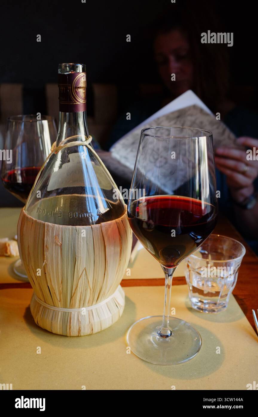 Una tradizionale bottiglia di Chianti e un bicchiere di vino alla Trattoria 4 Leoni Tuscan Restaurant, Firenze/Firenze, Italia Foto Stock