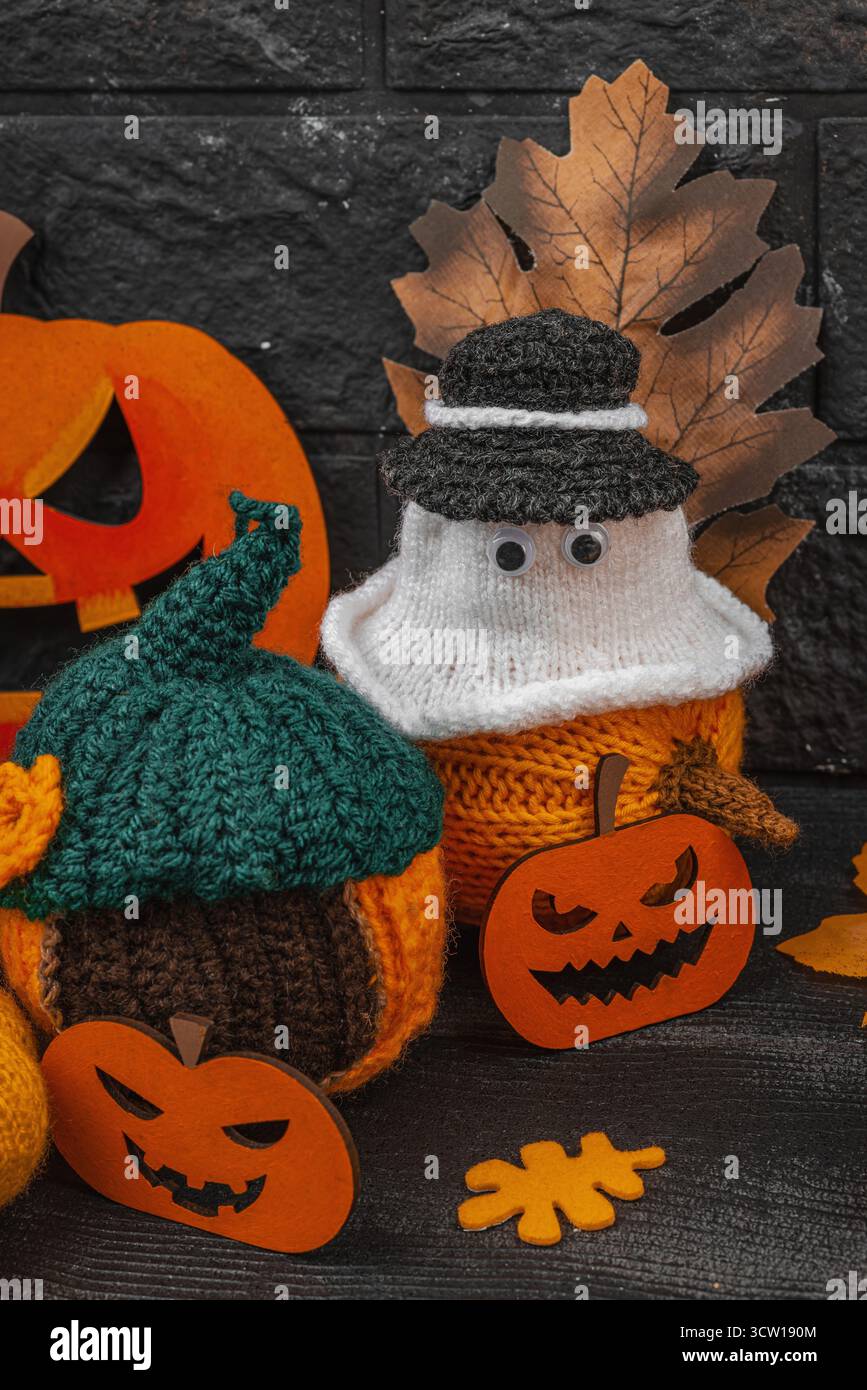 Accogliente scena di Halloween con graziose statuette di fantasmi in piccoli cappelli. Decorazioni autunnali lavorate a mano, zucche all'uncinetto, foglie autunnali, bacche, ragni, e gho Foto Stock
