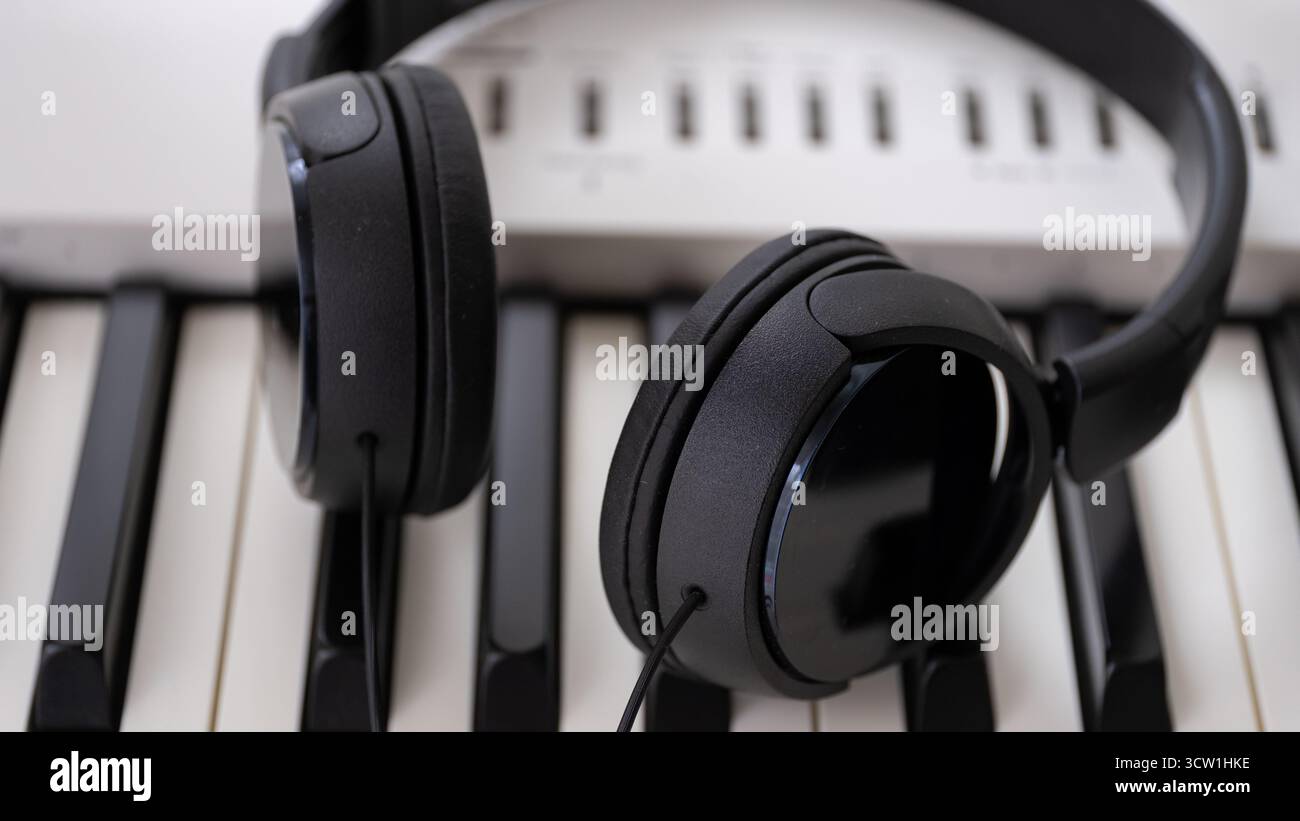Primo piano di cuffie nere appoggiate su una tastiera digitale per pianoforte, che simboleggia la creazione di musica moderna, la registrazione audio e l'apprendimento online. Ideale per me Foto Stock