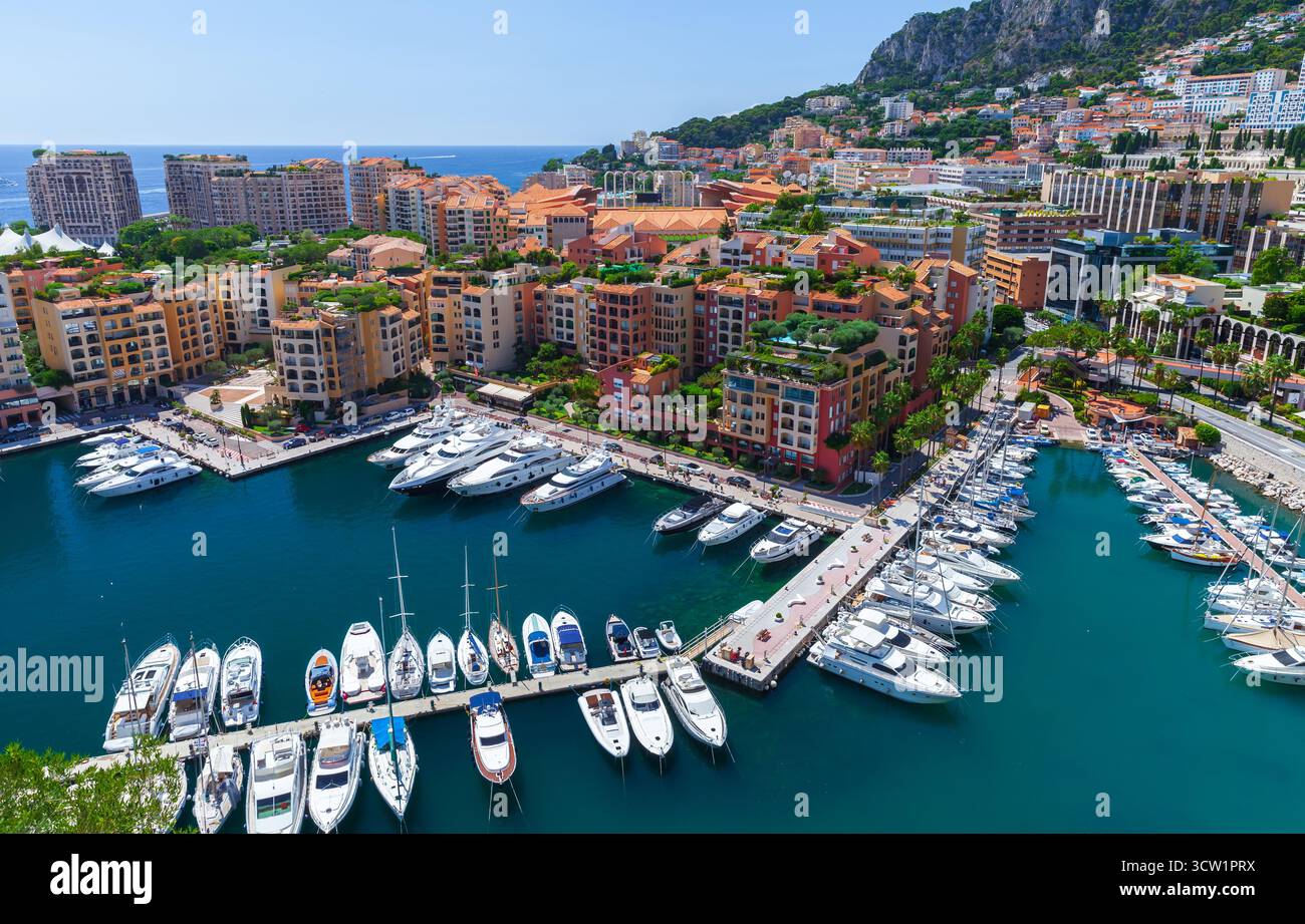 Vivace scenario portuale con numerosi yacht attraccati in un vivace porticciolo, edifici mediterranei illuminati dal sole che si arrampicano sulla collina e un mare cristallino Foto Stock