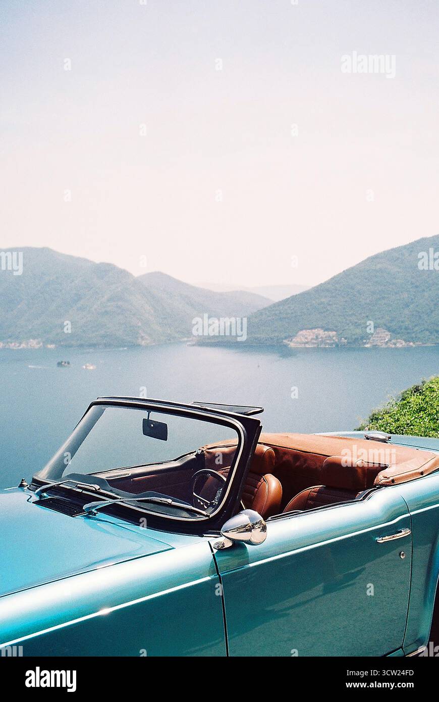 Foto analogica da 35 mm del turchese anni '1970 convertibile su un punto panoramico soleggiato in Montenegro, che si affaccia sulla baia e sulle colline. Nessun marchio di auto visibile. Foto Stock
