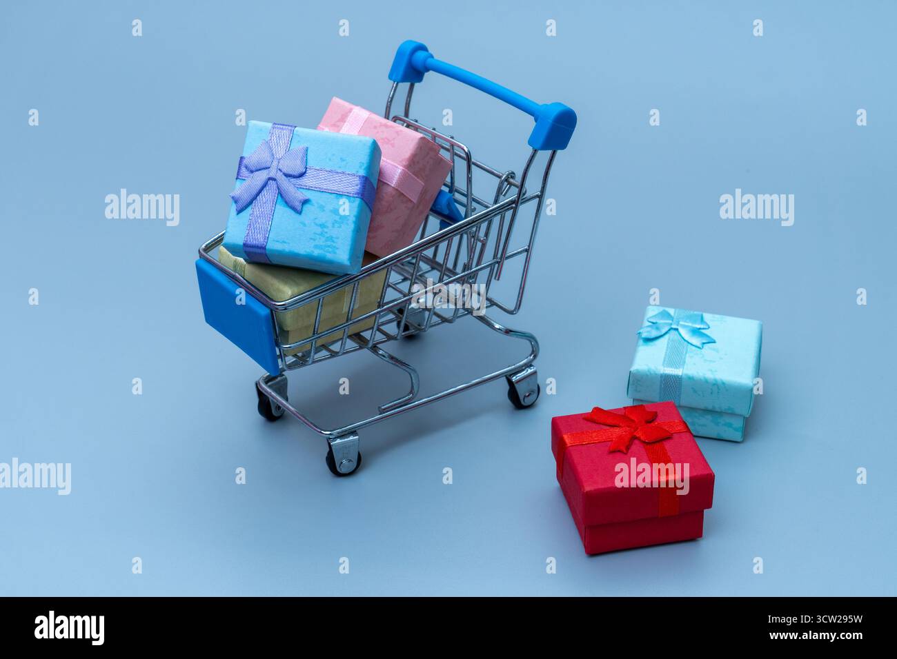 Mini carrello pieno di scatole regalo colorate su sfondo blu. Shopping online, vendita al dettaglio, vendite natalizie e concetto di acquisto consumer. Foto Stock
