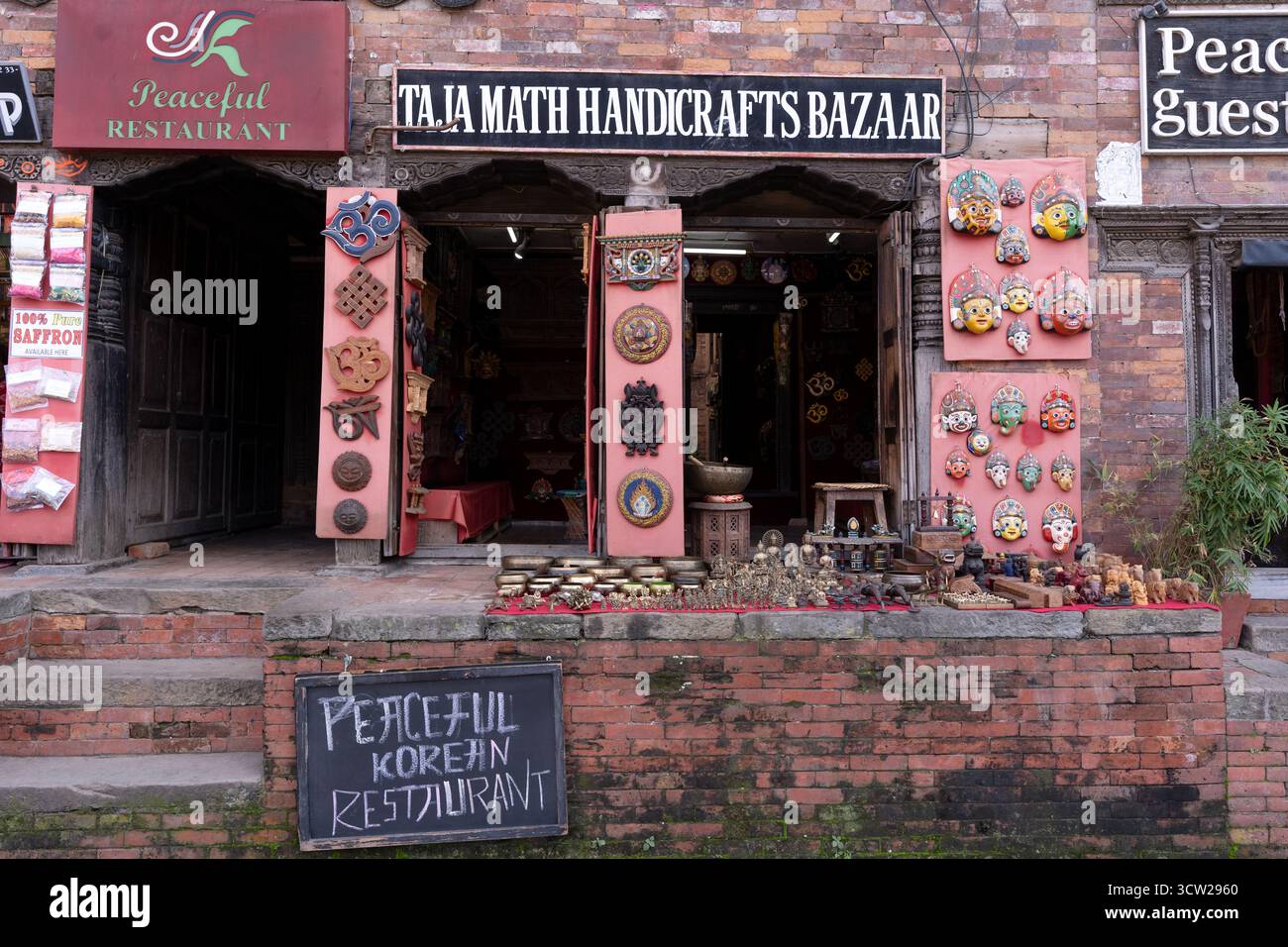 Rustico edificio in mattoni nepalesi con porte in legno ornamentali, maschere colorate e artigianato al Taj Math Handcrafts Bazaar Foto Stock