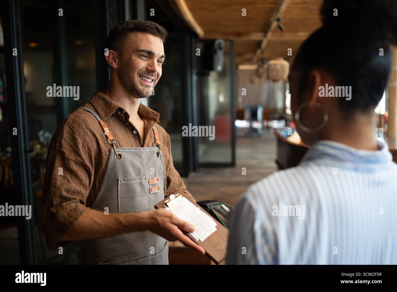 Orgoglioso proprietario di un caffè che si trova con fiducia dietro il bancone, pronto a servire i clienti con un sorriso caldo Foto Stock