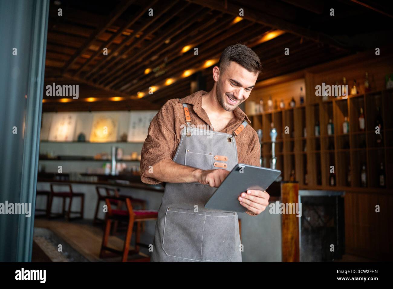 Orgoglioso proprietario di un caffè che si trova con fiducia dietro il bancone, pronto a servire i clienti con un sorriso caldo Foto Stock