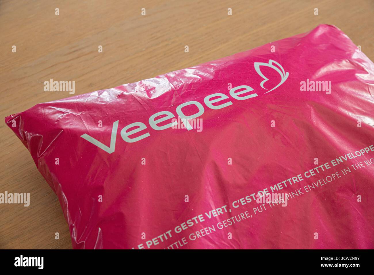 Una busta Veepee rosa con il logo del marchio in primo piano, appoggiata su una superficie in legno. Il testo incoraggia lo smaltimento ecocompatibile con un biling Foto Stock