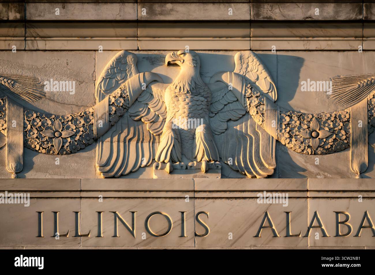 Lincoln Memorial Eagle Sculpture Washington DC // WASHINGTON DC - Una dettagliata scultura di aquila in marmo è visibile sulla facciata meridionale del Lincoln Memorial, illuminata dagli ultimi raggi dorati di luce prima del tramonto. Quest'aquila è una delle due sculture di rilievo all'esterno del monumento nazionale. Sotto l'aquila scolpita, sono iscritti nomi di stati statunitensi, come "ILLINOIS" e "ALABAMA". Questi rappresentano i 48 stati al momento della dedica del memoriale nel 1922, in onore di Abraham Lincoln. Foto Stock