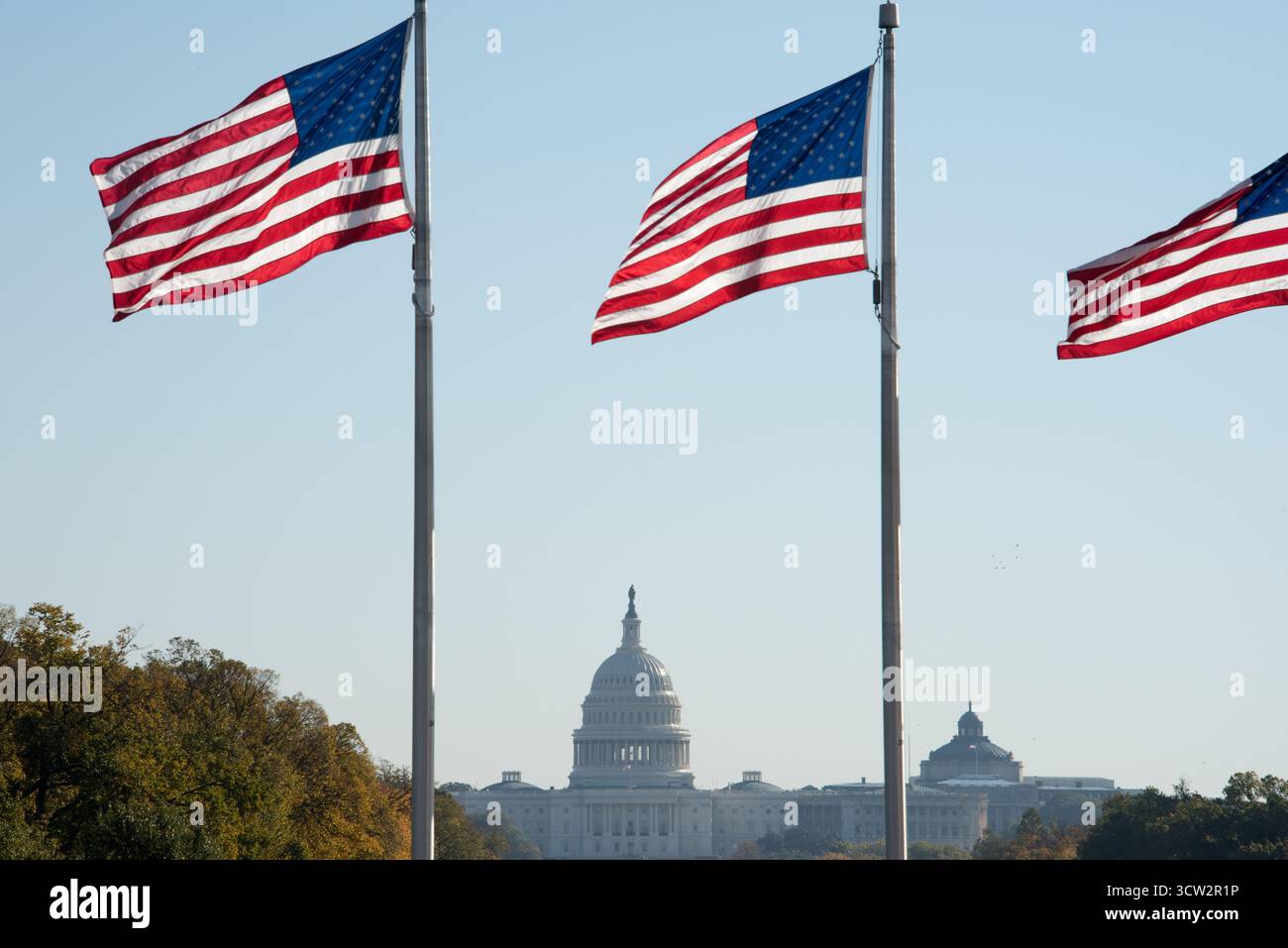 Edificio del Campidoglio degli Stati Uniti Washington DC // WASHINGTON DC - l'iconico Campidoglio degli Stati Uniti è visto sullo sfondo, parzialmente oscurato da diverse bandiere americane che sventolano su bandiere. Questo importante punto di riferimento a Capitol Hill è il luogo di incontro del Congresso degli Stati Uniti, che funge da sede del ramo legislativo del governo federale degli Stati Uniti. L'edificio è rinomato per la sua caratteristica architettura neoclassica e la grande cupola, che ospita sia il Senato che la camera dei rappresentanti. È un potente simbolo della democrazia americana e un significativo sito storico nel Foto Stock