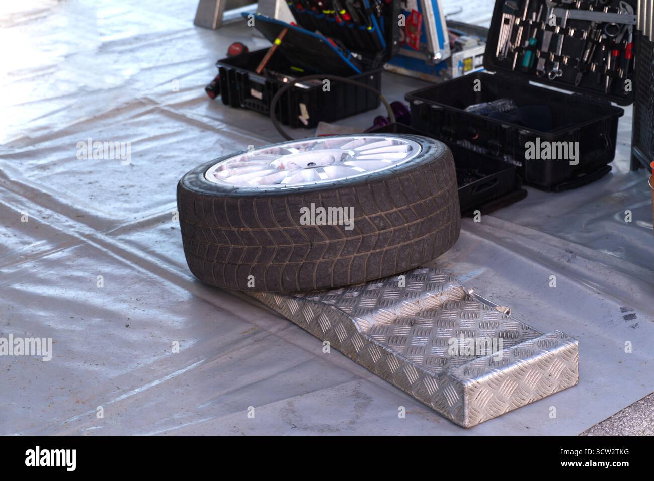 Lo pneumatico dalle prestazioni a basso profilo con cerchi bianchi in lega a più razze poggia sul pavimento dell'officina. Foto Stock