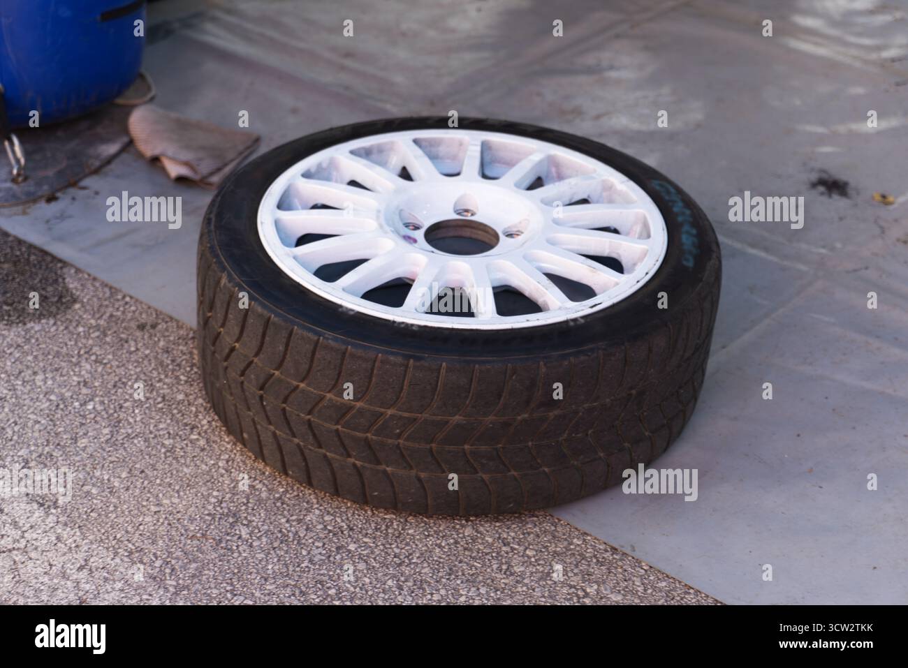Lo pneumatico dalle prestazioni a basso profilo con cerchi bianchi in lega a più razze poggia sul pavimento dell'officina. Foto Stock
