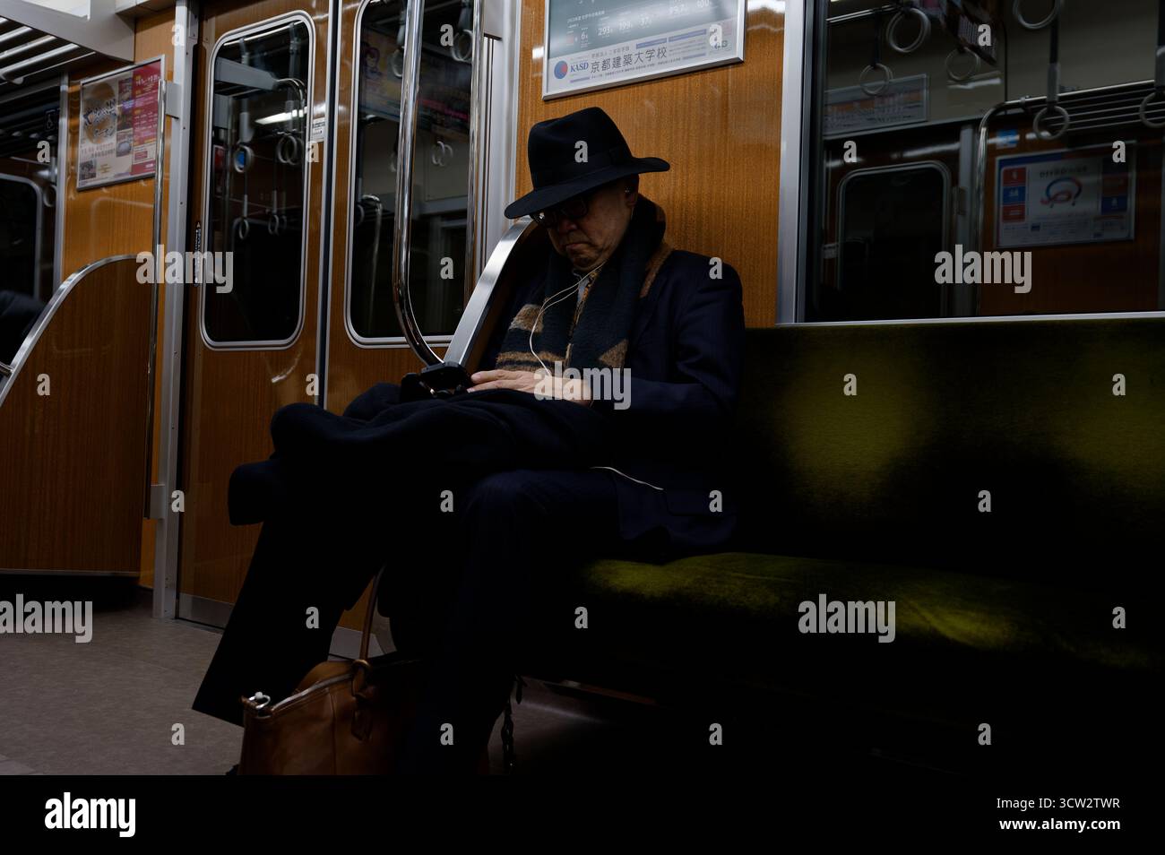 Un gentiluomo con un cappello e una tuta scura riposa tranquillamente su un treno della metropolitana di Osaka, illuminato da una luce soffusa dell'interno Foto Stock
