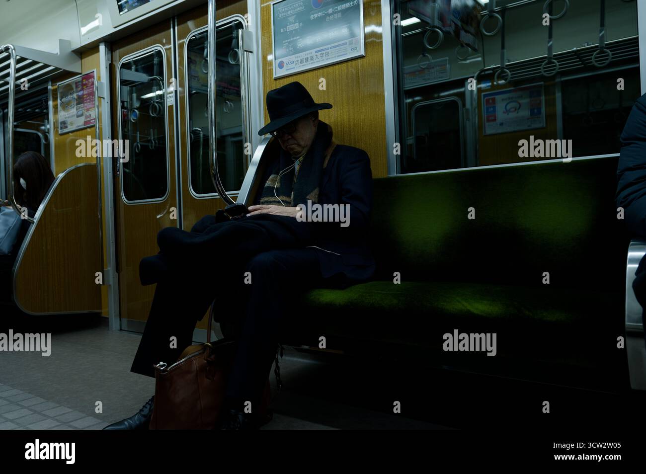 L'anziano con un abito scuro e un cappello riposa tranquillamente su un treno della metropolitana di Osaka Foto Stock