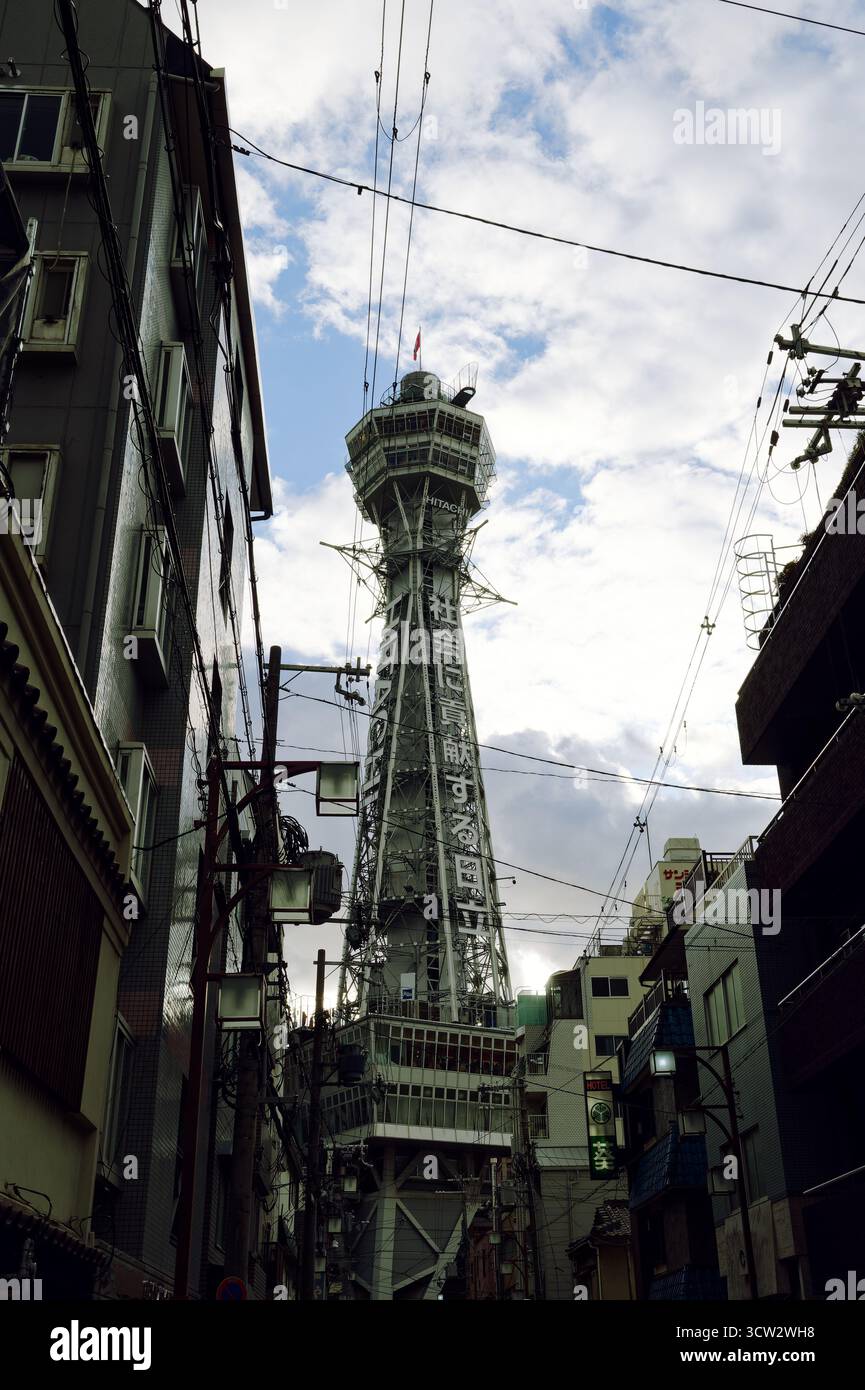 Torre Tsutenkaku incorniciata da strette strade di Osaka sotto un cielo luminoso e striato di nuvole Foto Stock