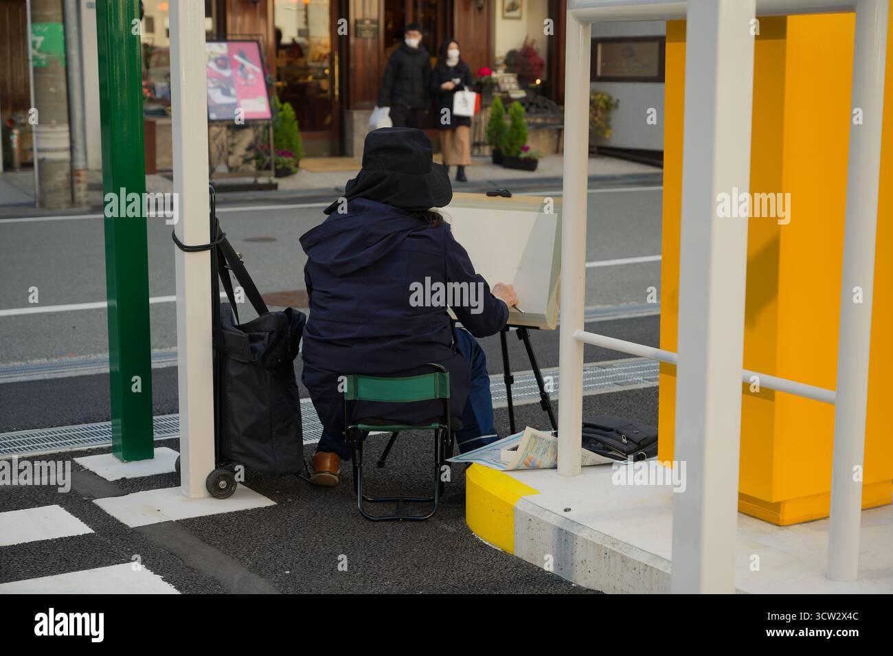Un pittore disegna tranquillamente in un parcheggio di Osaka, di fronte a un accogliente caffè del cioccolato in un fresco pomeriggio Foto Stock