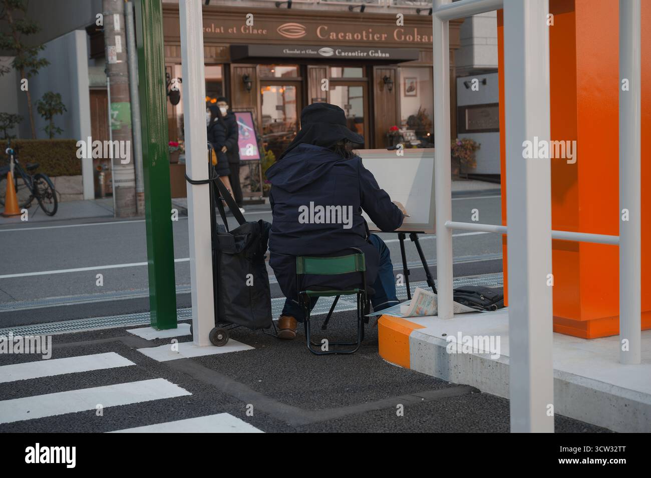 Il pittore siede in un parcheggio a Osaka, disegnando la vivace scena di strada di fronte a un caffè mentre passeggia accanto. Foto Stock