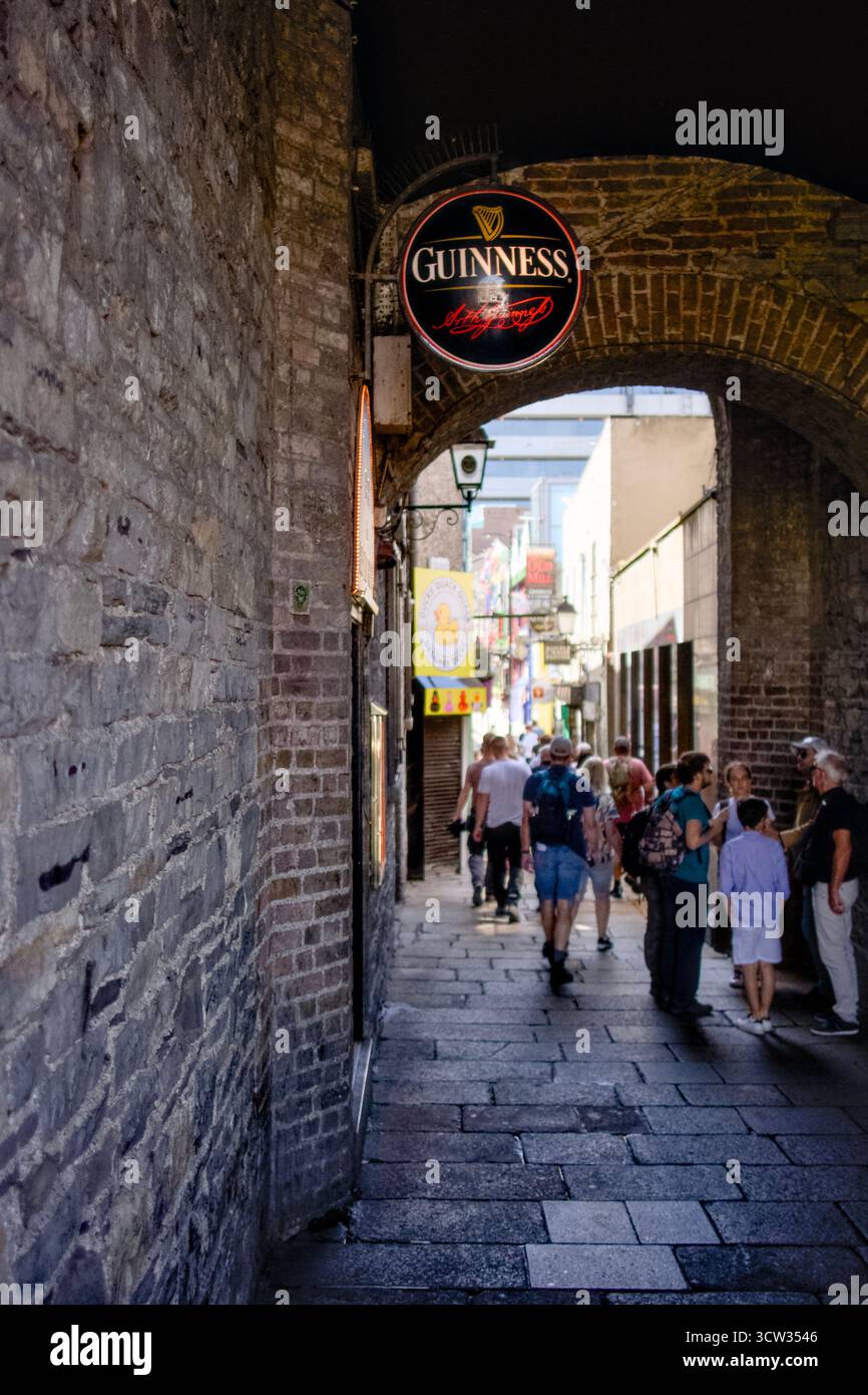I turisti camminano attraverso un vicolo stretto sotto un cartello Guinness nel quartiere Temple Bar di Dublino, Irlanda. Foto Stock