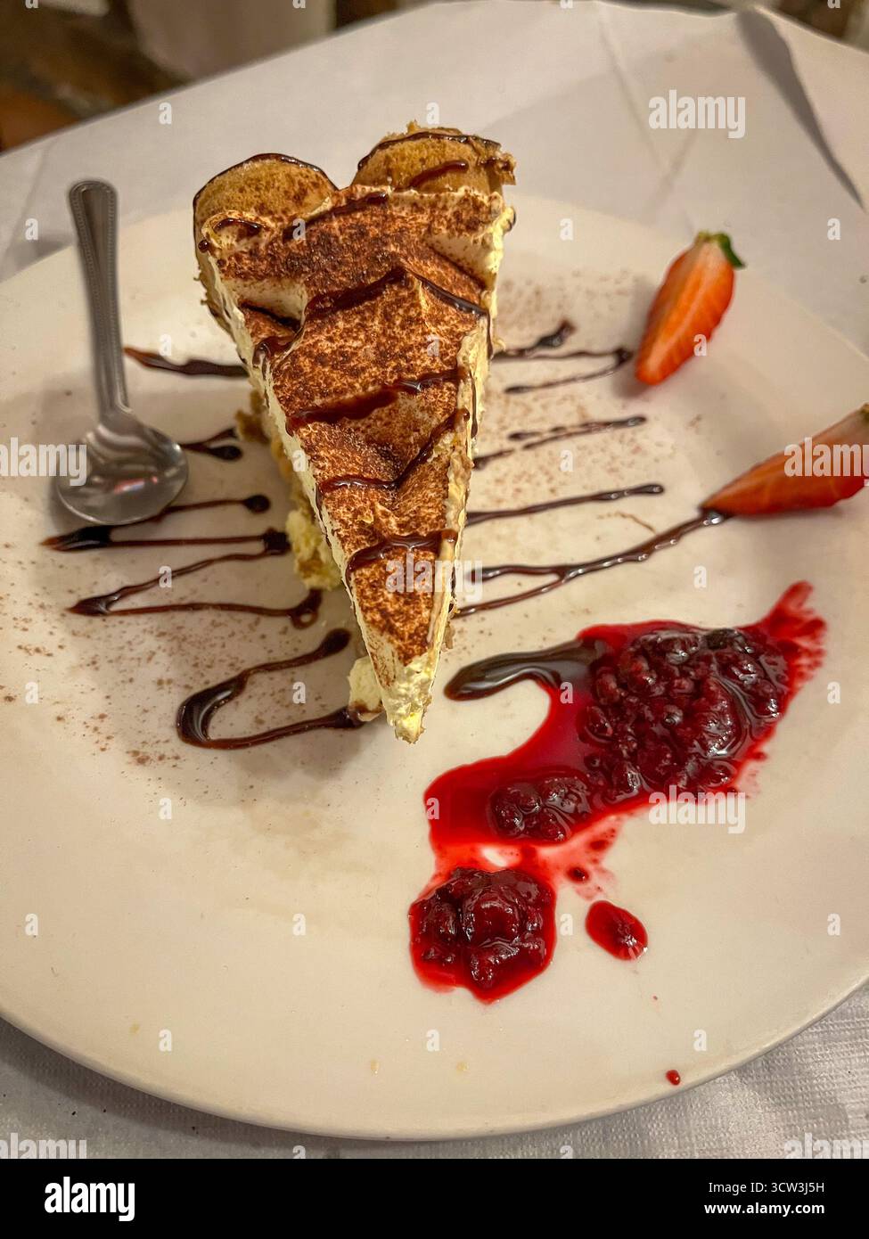 Elegante dessert tiramisù con gocciolatoio di cioccolato e fragole fresche in un ambiente ristorante - Immagine stock catturata con smartphone