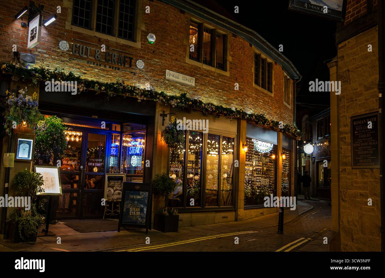 Accogliente pub tradizionale in un angolo di strada poco illuminato che emana calore e fascino invitante con luci decorative e facciata in mattoni Cut & Craft York 2024 Foto Stock