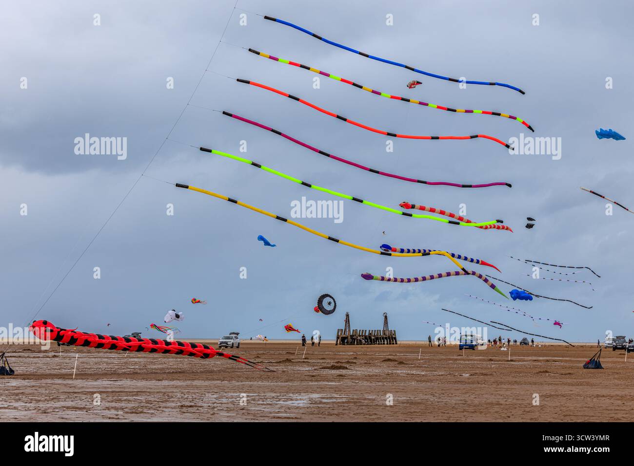 divertiti con gli aquiloni colorati con lunghe code che riempiono il cielo sopra l'ampia spiaggia sabbiosa al festival degli aquiloni di st annes di fronte all'estremità in legno del molo Foto Stock
