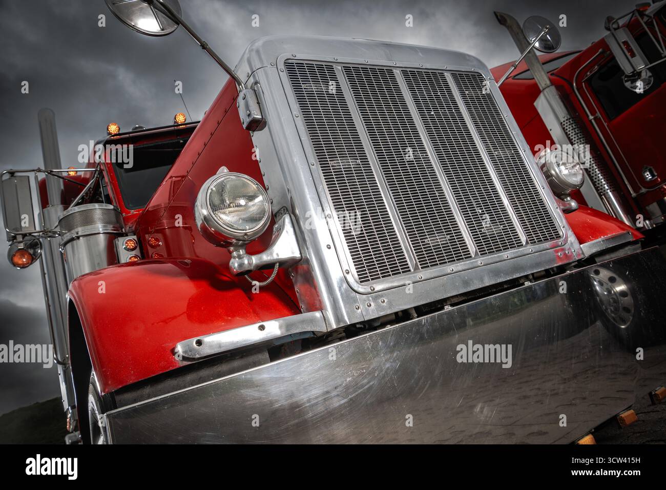 Due classici camion rossi si stagliano su un cielo scuro e nuvoloso, mostrando i loro dettagli cromati lucidi e il design potente durante un pomeriggio tranquillo. Foto Stock