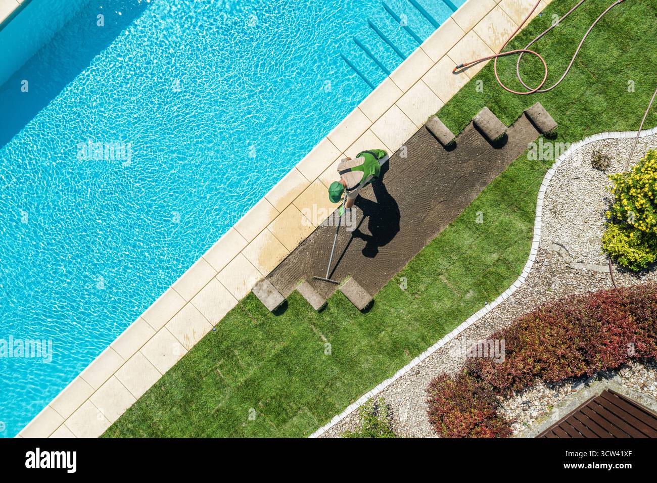 Un lavoratore tende al prato posato accanto a una piscina limpida in una giornata di sole, garantendo uno spazio all'aperto pulito e vivace per il relax. Foto Stock