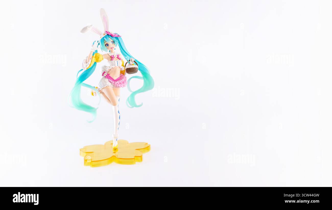 La bambola anime colorata presenta capelli blu e orecchie conigliette, che reggono dolcetti mentre si trova su una base gialla, incarnando un'atmosfera stravagante e giocosa Foto Stock