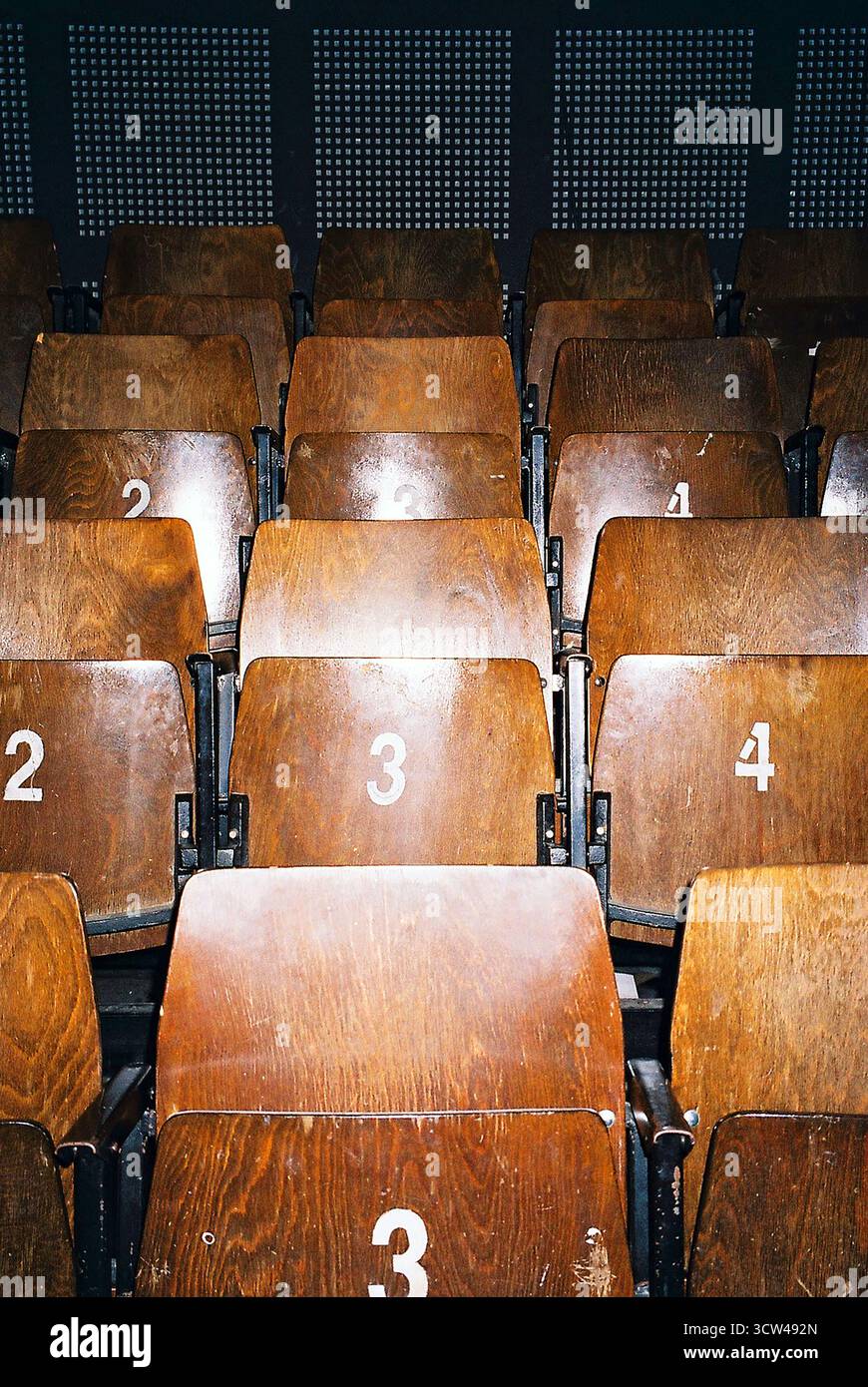 Fila di sedie pieghevoli in legno duro su un piccolo palcoscenico teatrale, catturate in stile analogico con illuminazione calda e composizione minimalista. Foto Stock