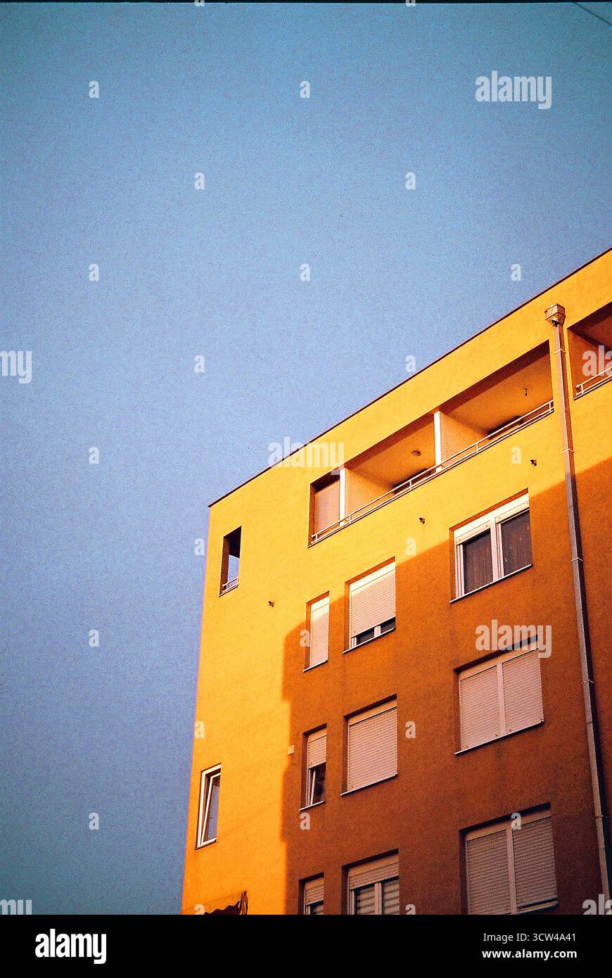 Un'immagine verticale di un edificio di appartamenti arancione al tramonto con l'ombra della struttura vicina, balconi e finestre visibili. Foto Stock