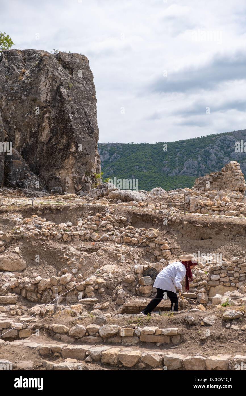 Amasya, Turchia - luglio 2022: Archeologi che lavorano presso antiche rovine di pietra con montagne, scenografiche nuvolose sullo sfondo del cielo. Persone che scavano in un sito roccioso Foto Stock