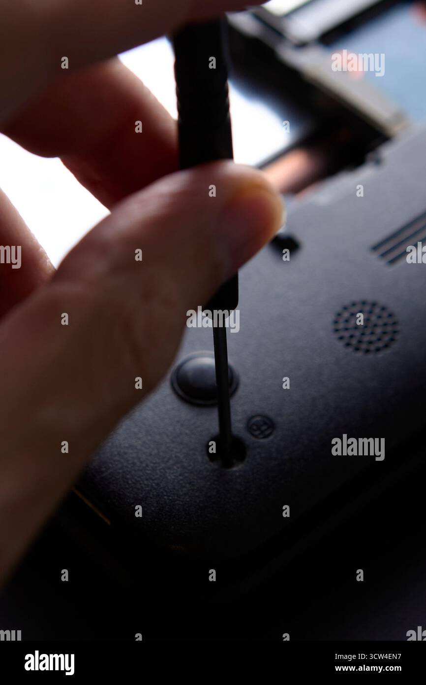 Foto macro di una persona che svita il pannello di un notebook con un cacciavite di precisione. Questo concetto di riparazione della tecnologia mostra i dettagli della manutenzione dei componenti elettronici Foto Stock