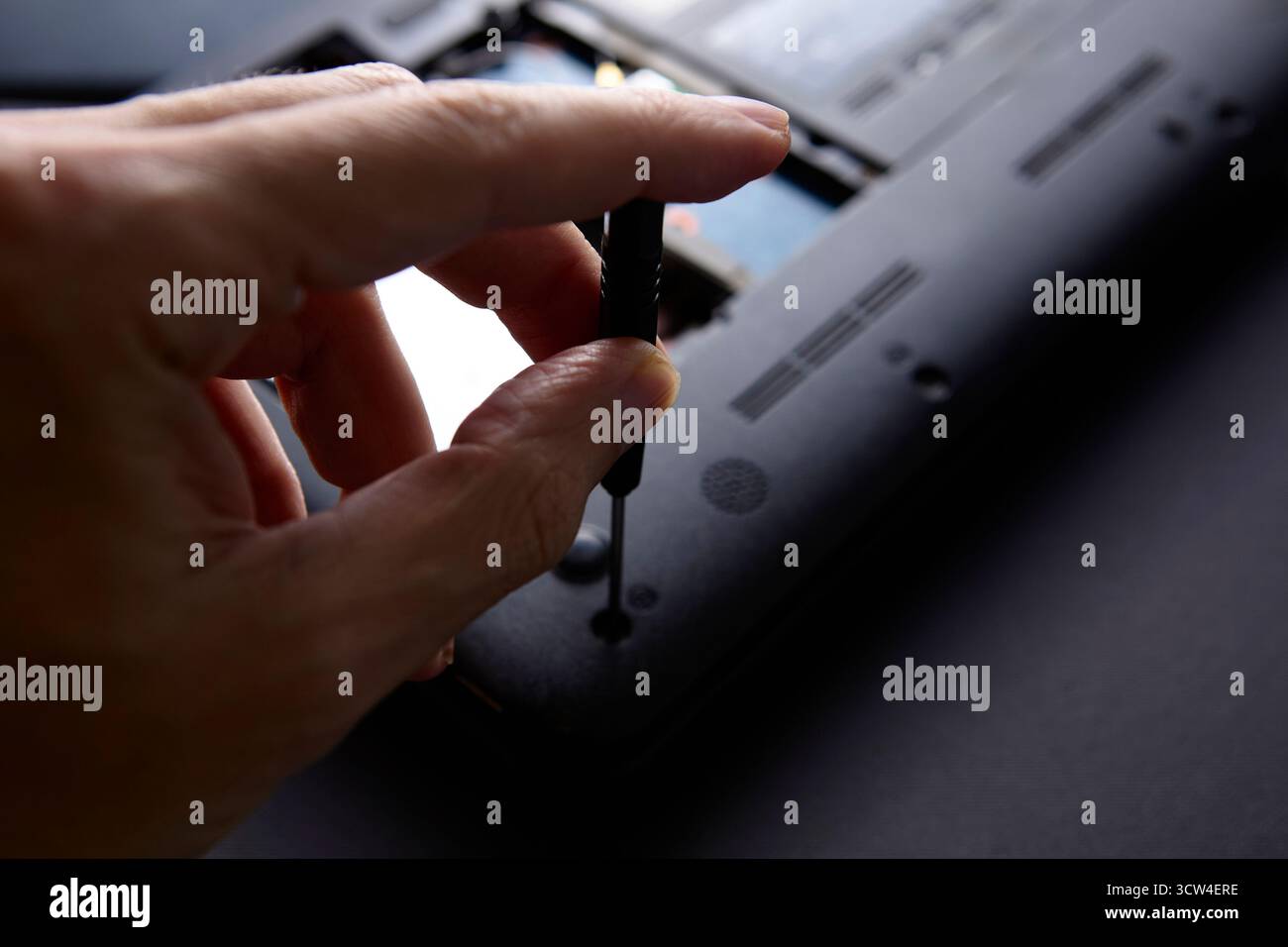 Una mano regge un cacciavite svitando il pannello posteriore di un computer portatile durante un processo di riparazione. La scena mette in evidenza la manutenzione della tecnologia e il re tecnico Foto Stock