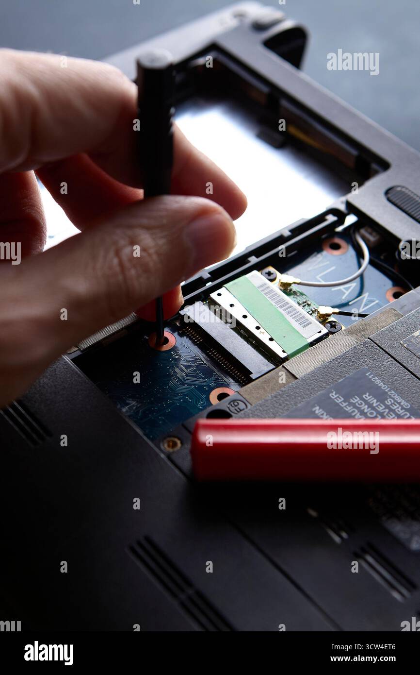 Primo piano di un tecnico che lavora a mano con un cacciavite e parti interne del computer portatile. Il processo di riparazione mostra il concetto di tecnologia, strumenti e professionisti Foto Stock