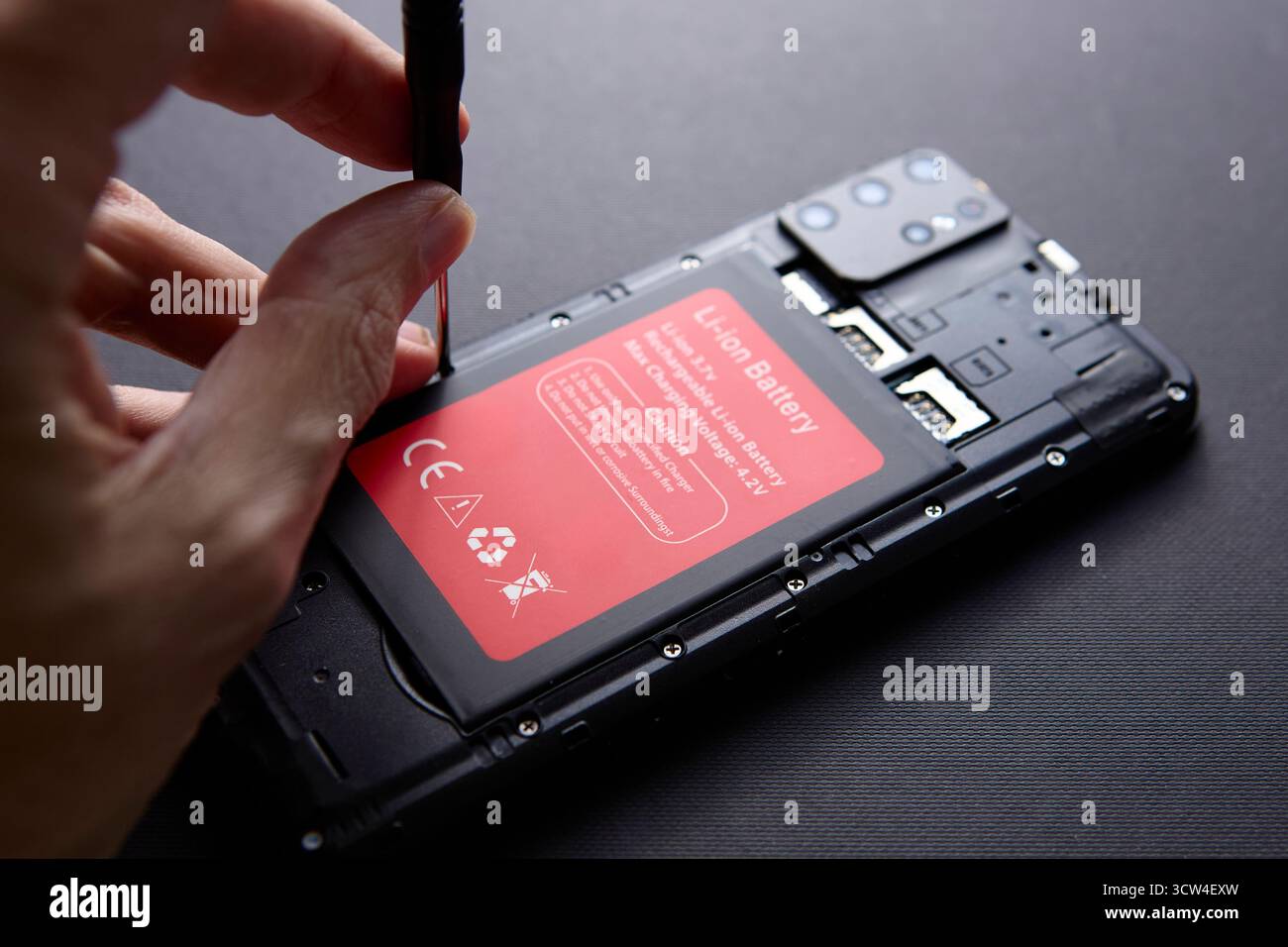 Primo piano di una persona che utilizza un cacciavite per aprire il coperchio posteriore dello smartphone su sfondo nero. Concetto di riparazione e manutenzione dei dispositivi mobili. Foto Stock