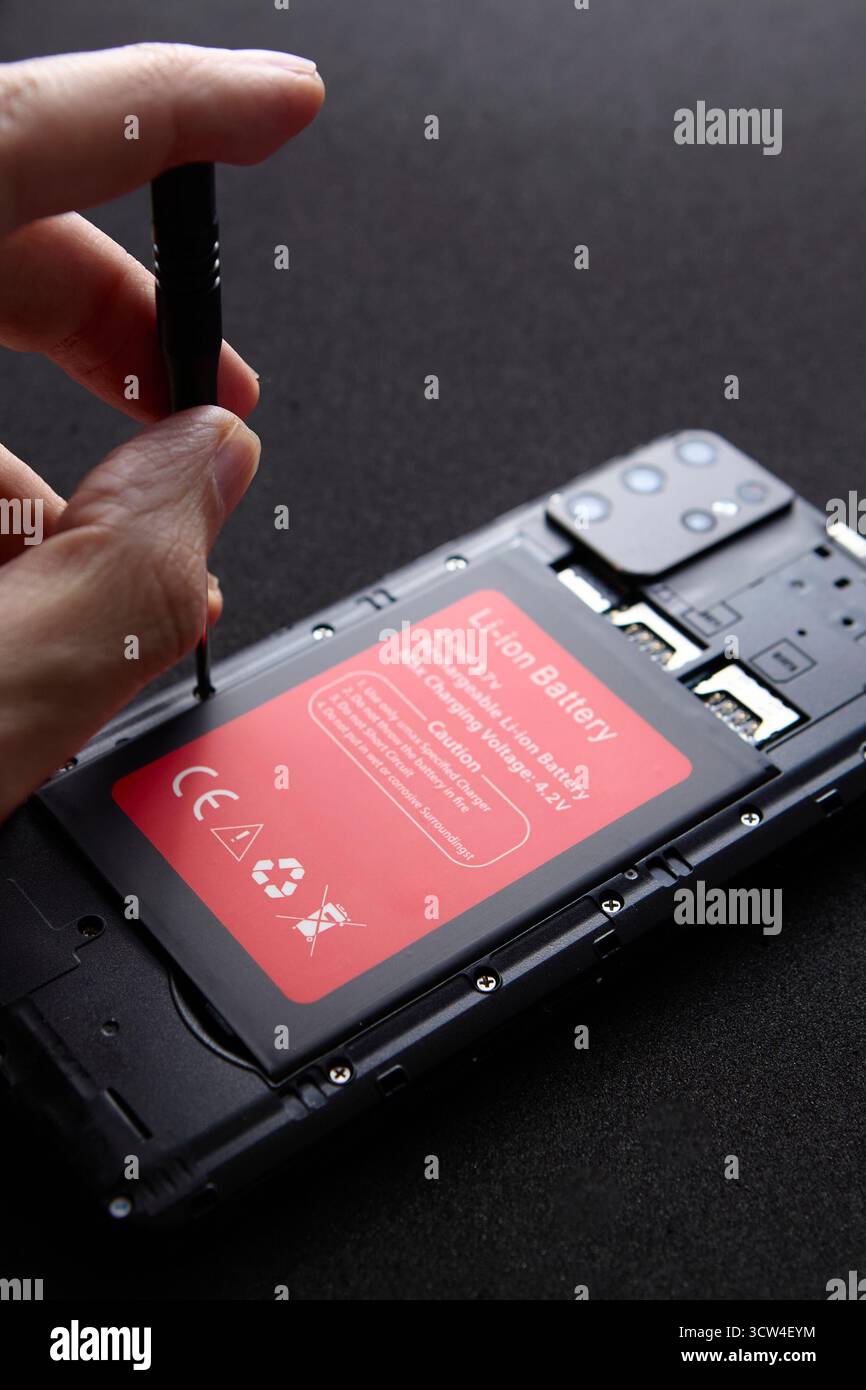 Primo piano delle mani del tecnico utilizzando un cacciavite per aprire lo smartphone per la sostituzione della batteria. L'immagine mostra il concetto di assistenza tecnica e riparazione p Foto Stock