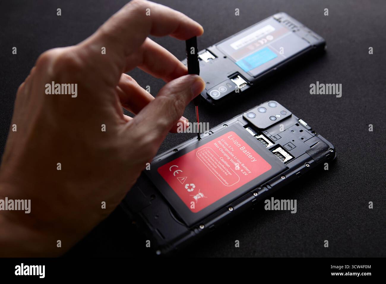 Una mano utilizza un cacciavite per aprire il dispositivo smartphone durante la manutenzione su superfici scure. La composizione minimale mostra un lavoro tecnico e un gadget precisi Foto Stock