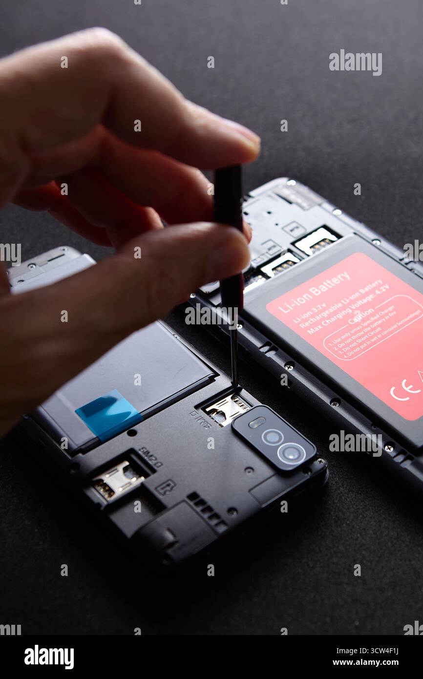 Primo piano di una mano di un tecnico utilizzando un cacciavite di precisione per riparare gli interni dello smartphone. La foto macro rappresenta un lavoro dettagliato nella manutenzione della tecnologia Foto Stock