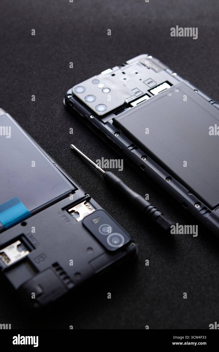 Smartphone smontato con schermo staccato e cacciavite su sfondo nero. La foto minimale rappresenta il concetto di riparazione e assistenza tecnologica Foto Stock