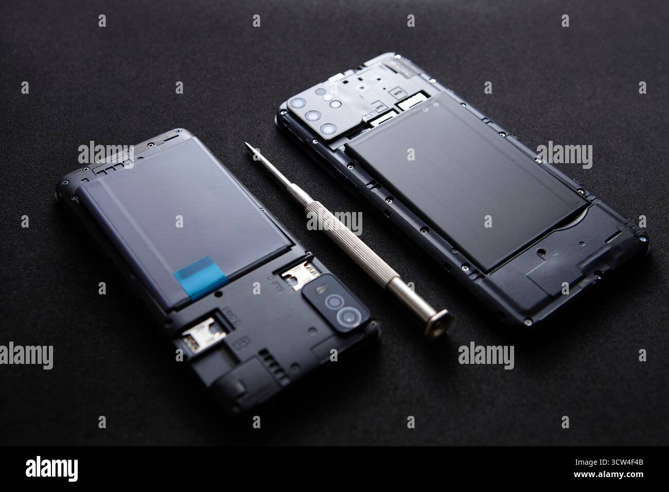 Smartphone con custodia aperta e cacciavite appoggiato sulla superficie nera. Foto concettuale che mostra gli strumenti di riparazione e la manutenzione dei dispositivi di precisione. Foto Stock