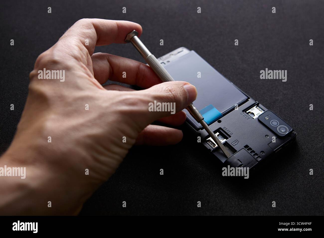 Un tecnico che utilizza un cacciavite per fissare o riassemblare i componenti dello smartphone. L'immagine evidenzia il processo di riparazione tecnico e l'attenzione ai dettagli. Foto Stock