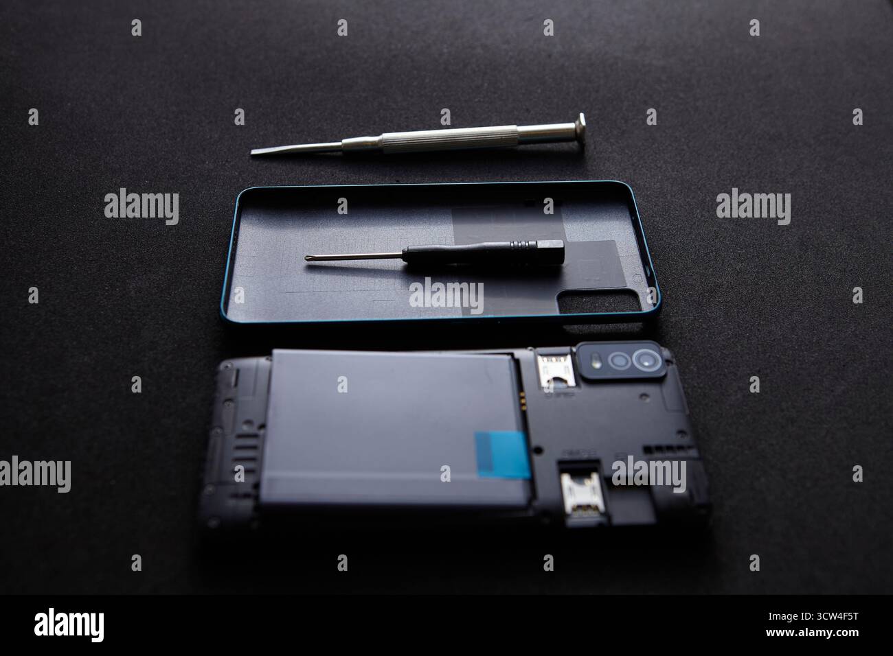 Uno smartphone smontato con cacciavite e utensili disposti in modo ordinato su sfondo scuro. La composizione minimalista mostra il concetto di riparazione tecnologica Foto Stock