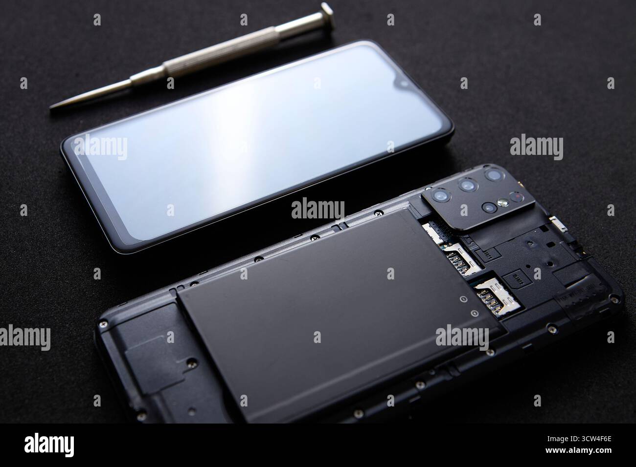 Uno smartphone con corpo aperto e un cacciavite posizionati accanto su una superficie nera riflettente. Immagine concettuale per il servizio di manutenzione e riparazione della tecnologia Foto Stock