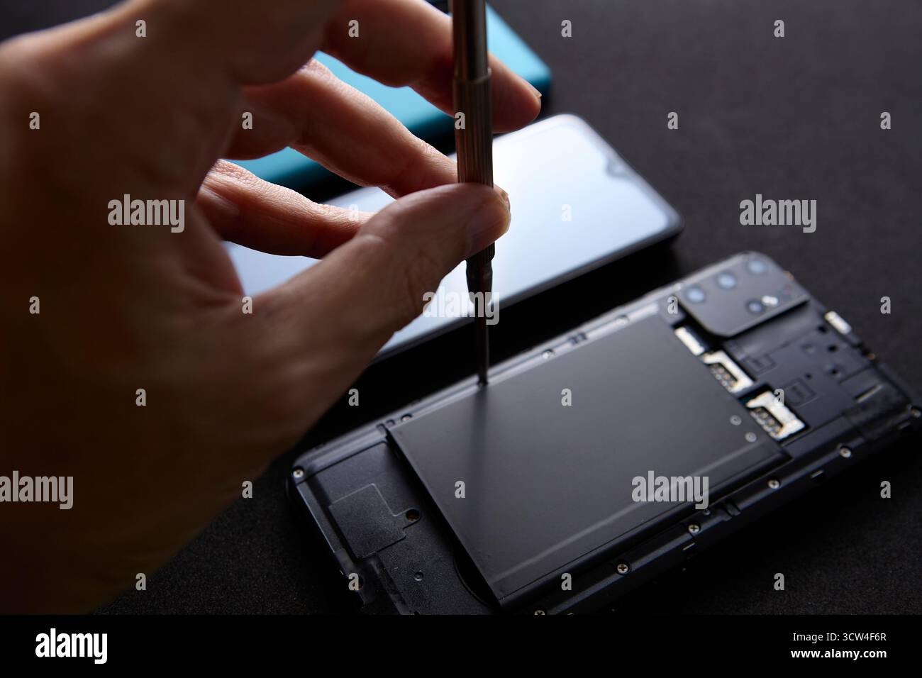 Primo piano del tecnico utilizzando un cacciavite per assemblare le parti dello smartphone. L'immagine mette in evidenza un lavoro accurato e preciso nella riparazione dei dispositivi mobili e nella manutenzione Foto Stock