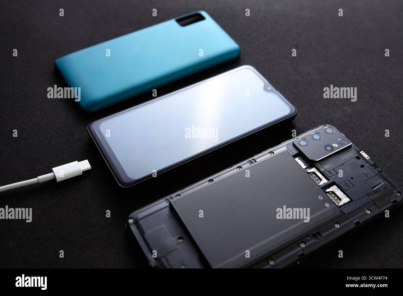 Uno smartphone fisso collegato al cavo di ricarica vicino a attrezzi di riparazione e parti di ricambio. La configurazione di studio rappresenta il completamento della manutenzione del dispositivo. Foto Stock