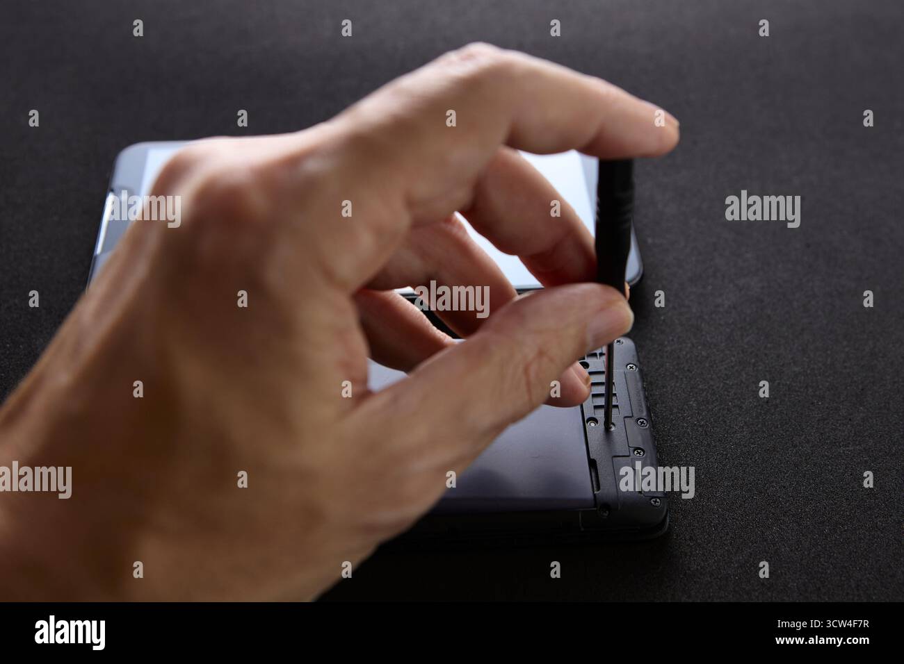 Primo piano di una mano che regola piccoli componenti all'interno di uno smartphone utilizzando strumenti di precisione. La foto cattura il lavoro dettagliato coinvolto nel dispositivo mobile Foto Stock
