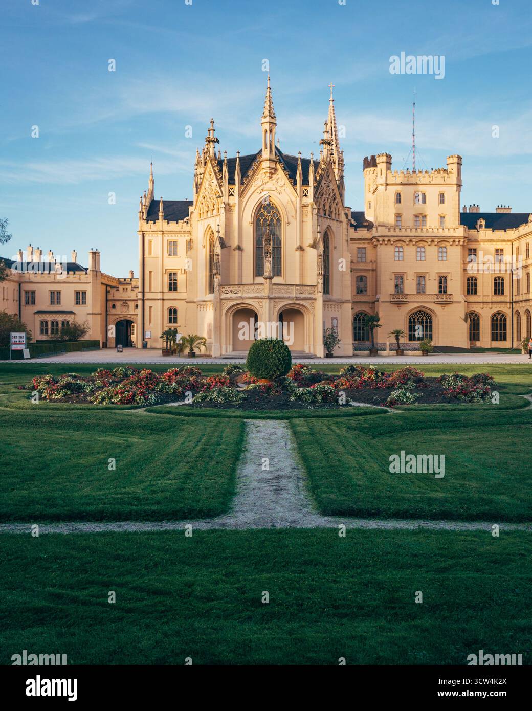 Uno splendido castello si erge maestosamente con un'architettura intricata, circondato da giardini ben tenuti e fiori colorati sotto un cielo blu cristallino. Foto Stock