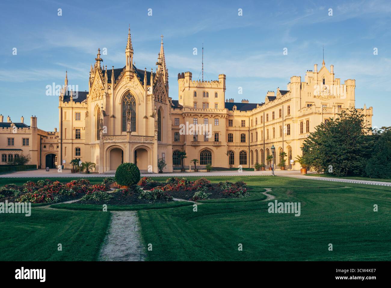 Uno splendido castello si erge alto sullo sfondo di un tramonto, circondato da giardini colorati e vegetazione lussureggiante. I visitatori possono esplorare la sua ricca architettura. Foto Stock