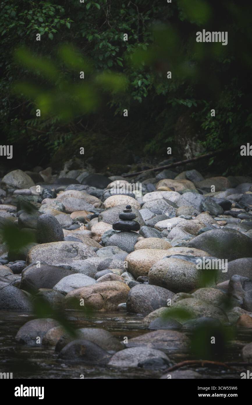 Pietre lisce e arrotondate sono accuratamente impilate l'una sull'altra lungo le rive di un fiume, circondate da un verde lussureggiante e dai suoni rilassanti Foto Stock